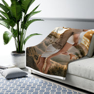 A printed throw blanket draped over a light gray sofa in a styled living room. The blanket features a photographic print of a couple embracing on a beach, with warm beige, brown, and white tones.