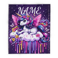 A square custom blanket or pillow cover featuring a colorful cartoon unicorn with pink wings, a gold horn, and flowers on a purple starry background. The word 'NAME' is printed at the top for personalization, with pink, blue, and yellow paint-drip effects below the unicorn.