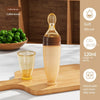 Coffee brown silicone baby bottle on a wooden cutting board with a glass of liquid.