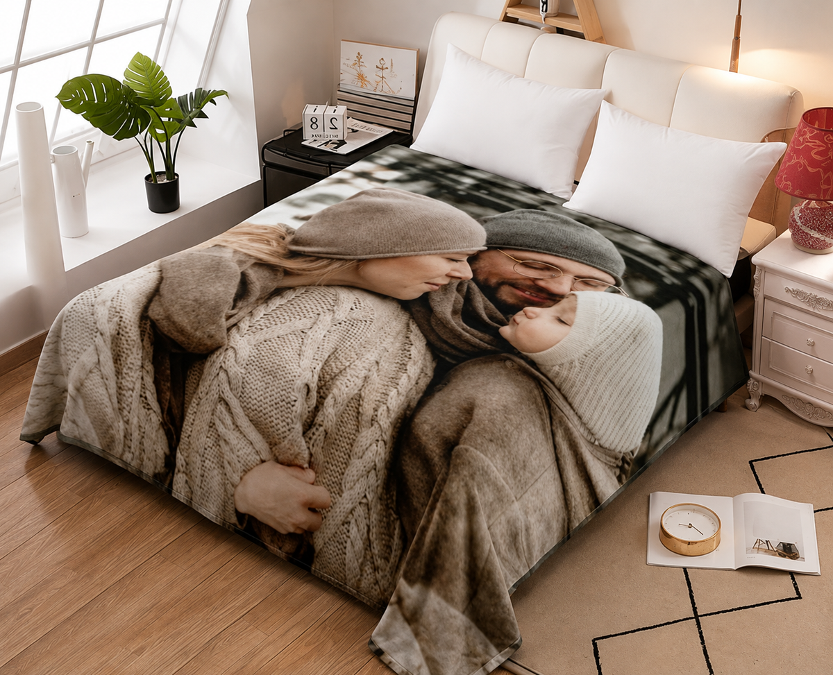 A bed in a styled bedroom featuring a large photographic print of a couple hugging under cozy sweaters and scarves. The bedding includes white pillows and a beige cable-knit throw blanket, set against a warm wood floor and bedside tables.