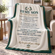 A cream-colored fleece blanket with a dark green and gold printed sentimental poem for a son, draped over a beige armchair in a cozy living room setting.