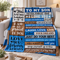 A fleece throw blanket draped over a light gray sofa in a living room setting. The blanket features a rustic wood-plank design with various blue, brown, and white panels containing motivational text for a son.