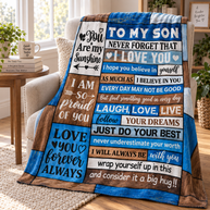 A patchwork-style emotional support blanket draped over a beige armchair in a bright living room. The blanket features multiple blue, brown, and white panels with motivational quotes addressed to a son, including 'You Are My Sunshine' and 'I Love You'.
