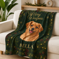 A personalized Christmas throw blanket draped over a white armchair in a living room setting. The blanket features a golden retriever portrait, the text 'Merry Weafmats' and 'BELLA' in gold, and a dark green background decorated with pine branches, red berries, and gold stars.