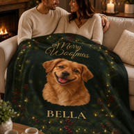 A couple sits on a couch wrapped in a dark green personalized Christmas blanket featuring a golden retriever portrait, gold 'Merry Woofmas' text, and the name 'BELLA'.
