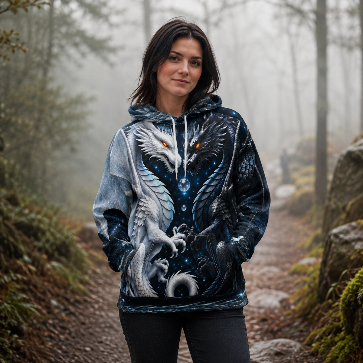 A woman stands on a misty forest path wearing a pullover hoodie with a highly detailed fantasy dragon print in shades of blue, gray, and white with glowing orange eyes.