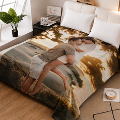 A custom printed blanket featuring a photo of a couple embracing, styled on a bed in a modern bedroom setting with wooden floors, bedside tables, and a potted plant.
